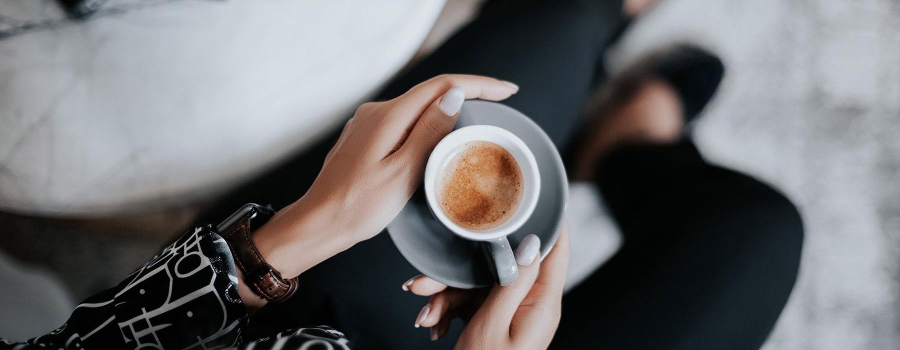 business woman sits next to a marble table with books and holds a saucer with a cup of espresso